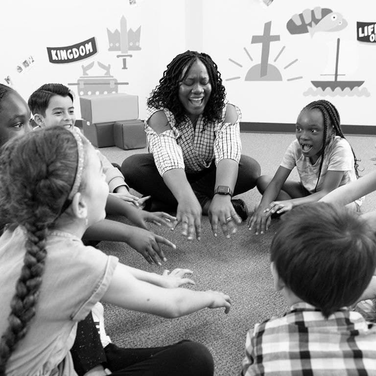 A volunteer sitting in a circle with children during kids church
